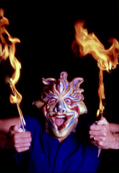 Fred Curchack performs the role of Ariel from Shakespeare's The Tempest. Man in spirit mask holding leaping flames.